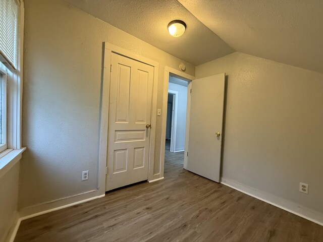 additional living space featuring a textured wall, lofted ceiling, wood finished floors, baseboards, and a textured ceiling