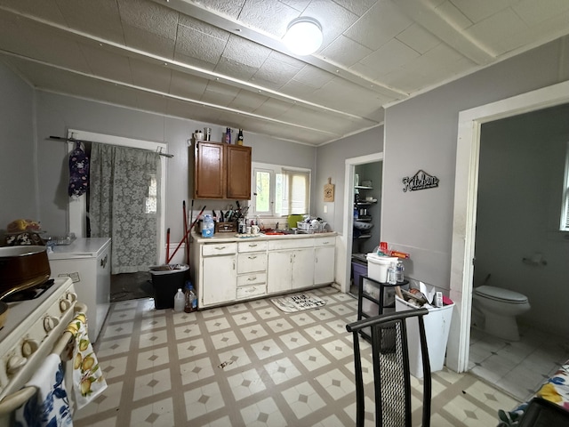 kitchen with brown cabinetry, light countertops, light floors, and white range with gas stovetop