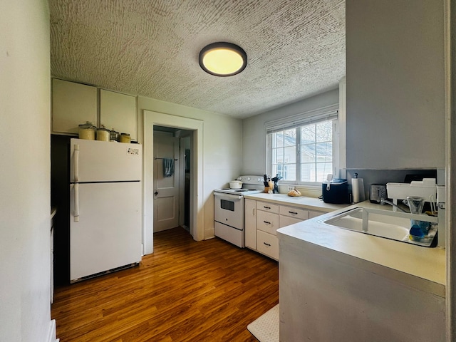 kitchen featuring a sink, a textured ceiling, dark wood-type flooring, white appliances, and light countertops