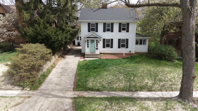 colonial house with a shingled roof, driveway, a chimney, and a front yard
