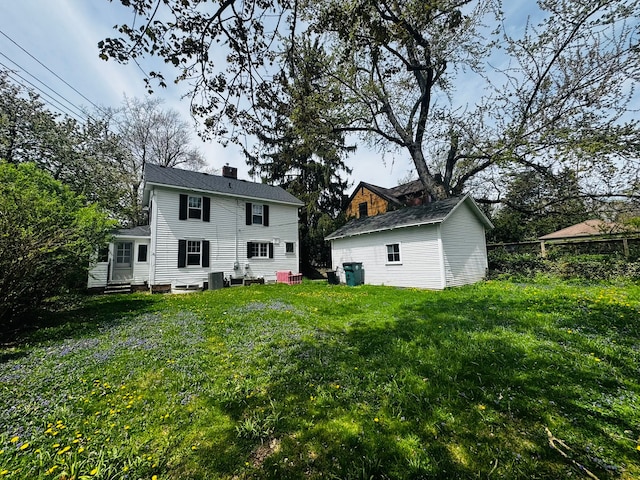 back of house featuring a chimney, entry steps, an outbuilding, and a lawn