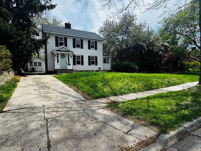colonial inspired home with an outdoor structure, driveway, a shed, a front lawn, and a chimney
