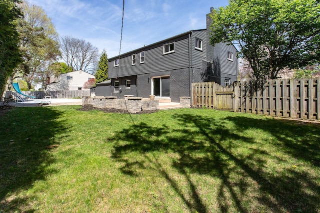 back of property with fence, a chimney, a lawn, and brick siding