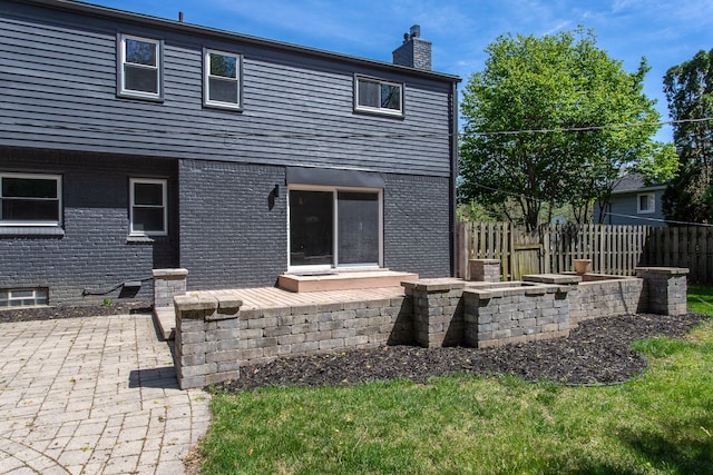 back of property with brick siding, a patio, fence, and a chimney