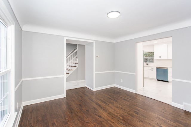 spare room featuring baseboards, a sink, wood finished floors, and stairway