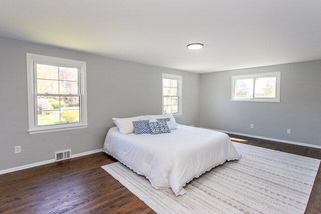 bedroom with visible vents, baseboards, dark wood-type flooring, and multiple windows