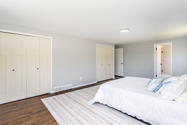 bedroom featuring baseboards, two closets, wood finished floors, and visible vents