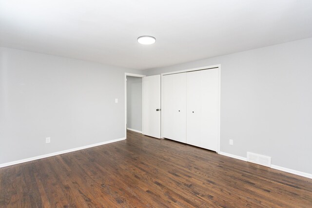 unfurnished bedroom with visible vents, baseboards, dark wood-type flooring, and a closet
