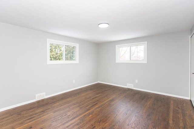 spare room featuring a healthy amount of sunlight, baseboards, dark wood-type flooring, and visible vents