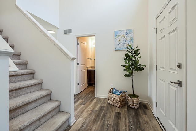 entryway with visible vents, stairs, a towering ceiling, wood finished floors, and baseboards