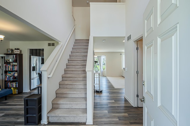 stairway with visible vents, wood finished floors, and a towering ceiling