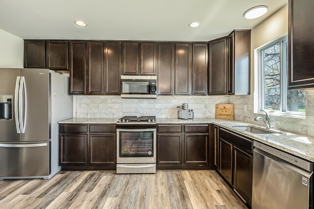 kitchen with dark brown cabinets, light stone countertops, light wood-style floors, a sink, and appliances with stainless steel finishes