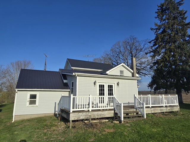 rear view of property with a lawn, a wooden deck, a chimney, and metal roof
