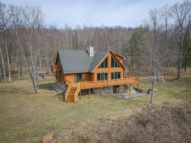 rear view of property with a lawn, a chimney, a deck, and a forest view
