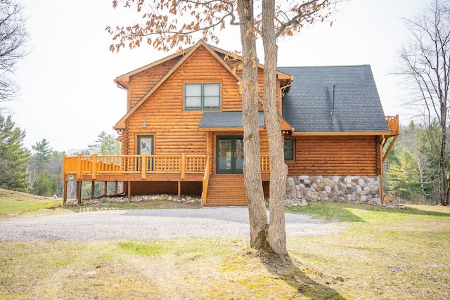 log cabin with a shingled roof, log exterior, a front lawn, and a deck