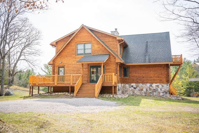 cabin featuring a shingled roof, a wooden deck, log exterior, a front yard, and a chimney