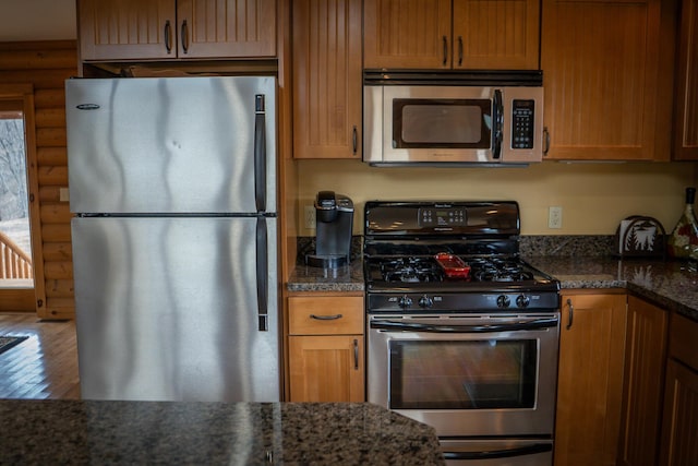 kitchen with dark stone countertops, appliances with stainless steel finishes, wood finished floors, and rustic walls