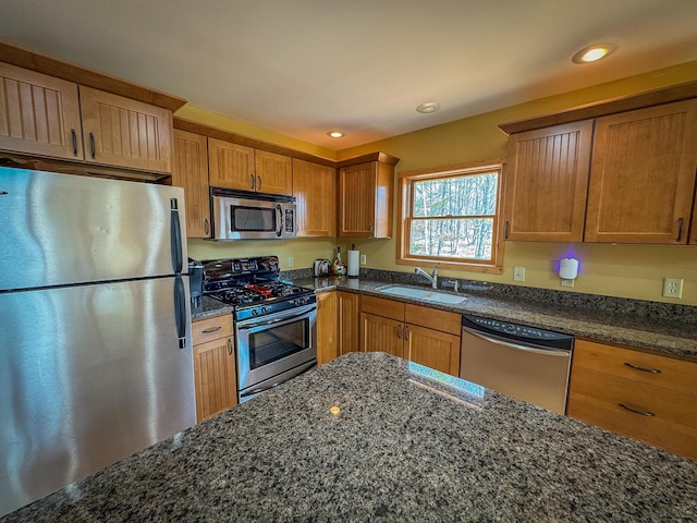 kitchen with brown cabinets, a sink, dark stone counters, stainless steel appliances, and recessed lighting