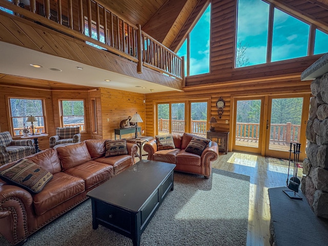 living area with a towering ceiling, rustic walls, a healthy amount of sunlight, and wood finished floors