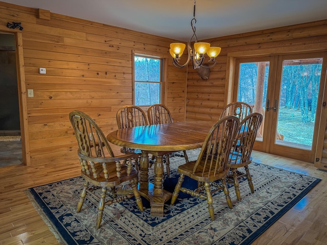 dining room with rustic walls, an inviting chandelier, french doors, and light wood-type flooring