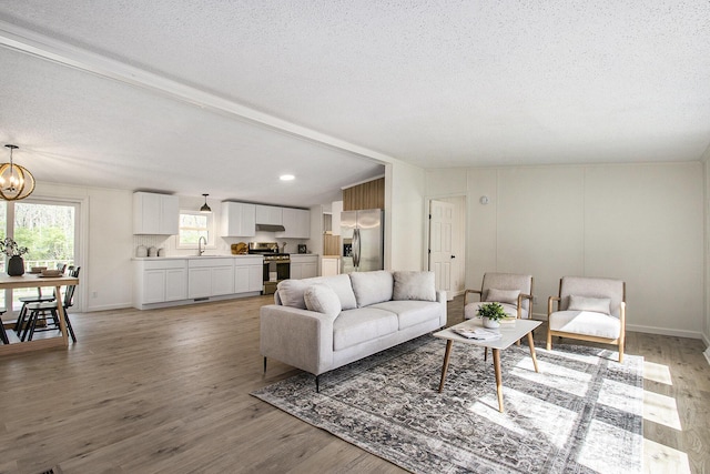 living area with lofted ceiling, light wood-type flooring, a textured ceiling, and a chandelier