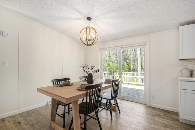dining space with light wood-style flooring, a textured ceiling, a chandelier, and ornamental molding