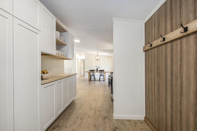 hall with baseboards, a textured ceiling, and light wood-style flooring