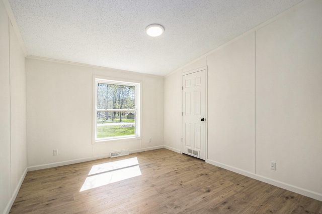 unfurnished room featuring a textured ceiling, visible vents, wood finished floors, and lofted ceiling