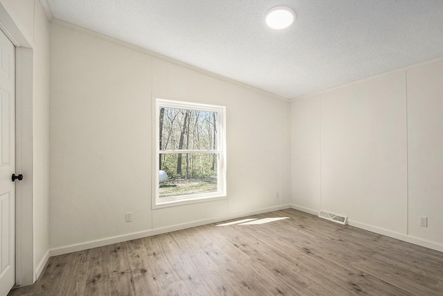 unfurnished room with visible vents, wood finished floors, baseboards, a textured ceiling, and vaulted ceiling