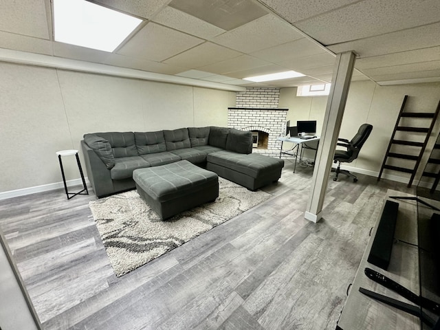 living room featuring wood finished floors, a brick fireplace, baseboards, and a drop ceiling