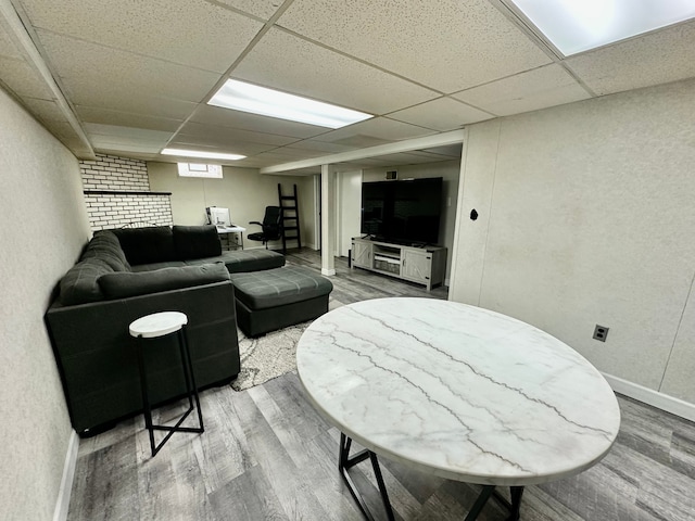 living area with a drop ceiling, a textured wall, baseboards, and wood finished floors