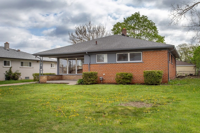rear view of house with brick siding, a shingled roof, a yard, and a chimney