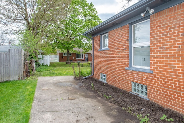 view of property exterior featuring fence, a yard, a patio area, and brick siding