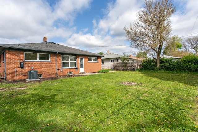 back of property with brick siding, central air condition unit, a yard, and a chimney