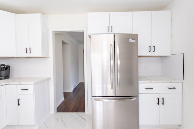 kitchen featuring light stone counters, freestanding refrigerator, white cabinets, and tasteful backsplash