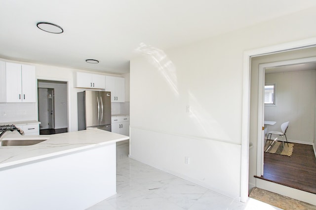 kitchen featuring white cabinets, light stone countertops, a sink, freestanding refrigerator, and decorative backsplash