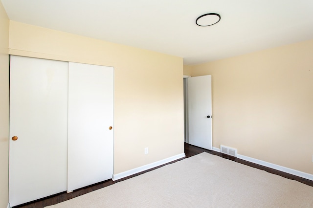 unfurnished bedroom featuring visible vents, dark wood finished floors, baseboards, and a closet