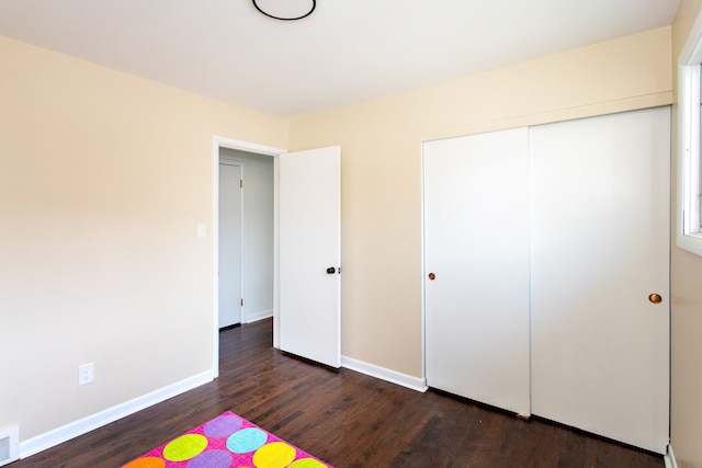 unfurnished bedroom featuring dark wood-type flooring, baseboards, visible vents, and a closet