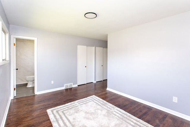 unfurnished bedroom with visible vents, baseboards, ensuite bath, and wood finished floors