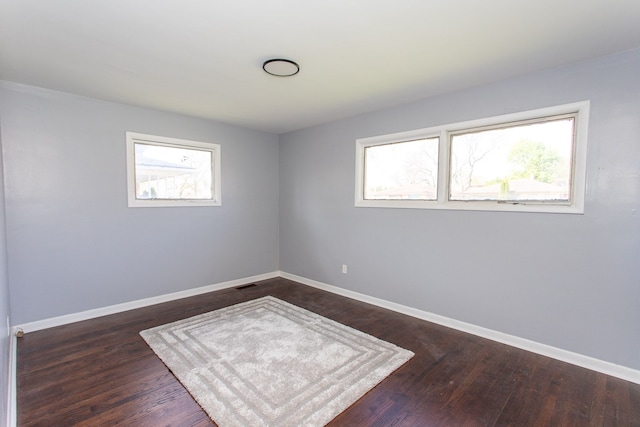 spare room with baseboards, dark wood-style floors, plenty of natural light, and visible vents