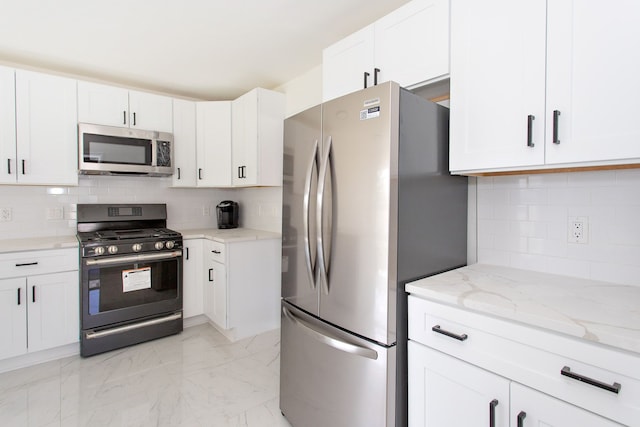 kitchen with light stone countertops, appliances with stainless steel finishes, marble finish floor, white cabinetry, and backsplash