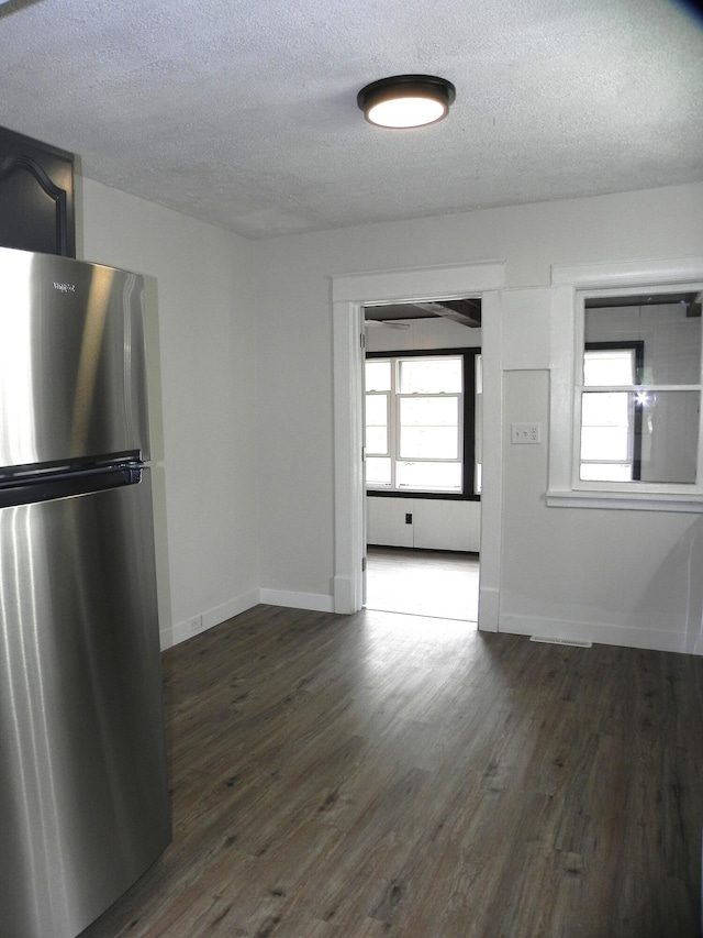 unfurnished dining area featuring baseboards, a textured ceiling, and dark wood finished floors
