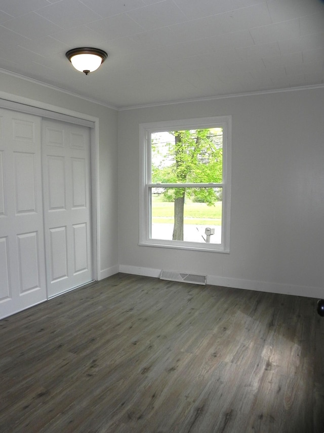 unfurnished bedroom featuring crown molding, dark wood-type flooring, visible vents, and a closet