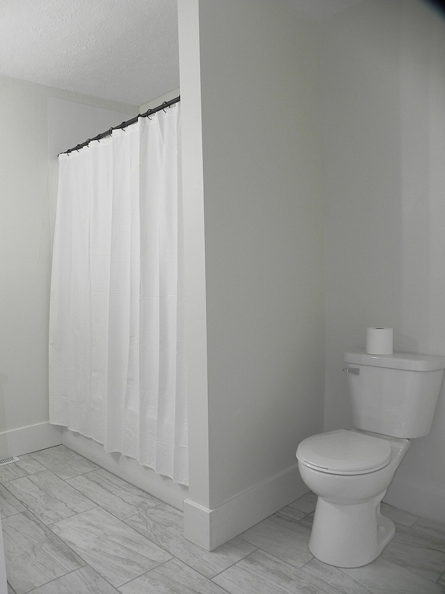 bathroom with a shower with curtain, a textured ceiling, baseboards, toilet, and marble finish floor