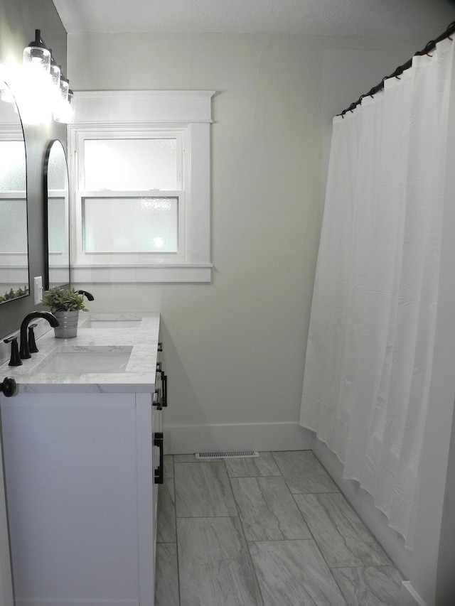 bathroom featuring visible vents, double vanity, marble finish floor, baseboards, and a sink