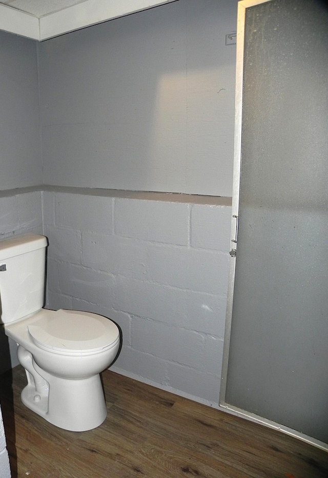 bathroom featuring concrete block wall, wood finished floors, and toilet