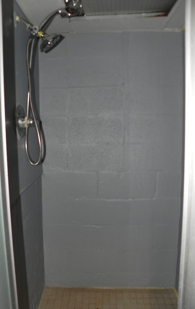 full bath featuring concrete block wall and tiled shower