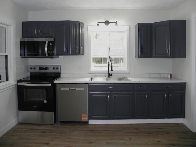 kitchen featuring dark wood-style flooring, light countertops, dark cabinetry, a sink, and stainless steel appliances