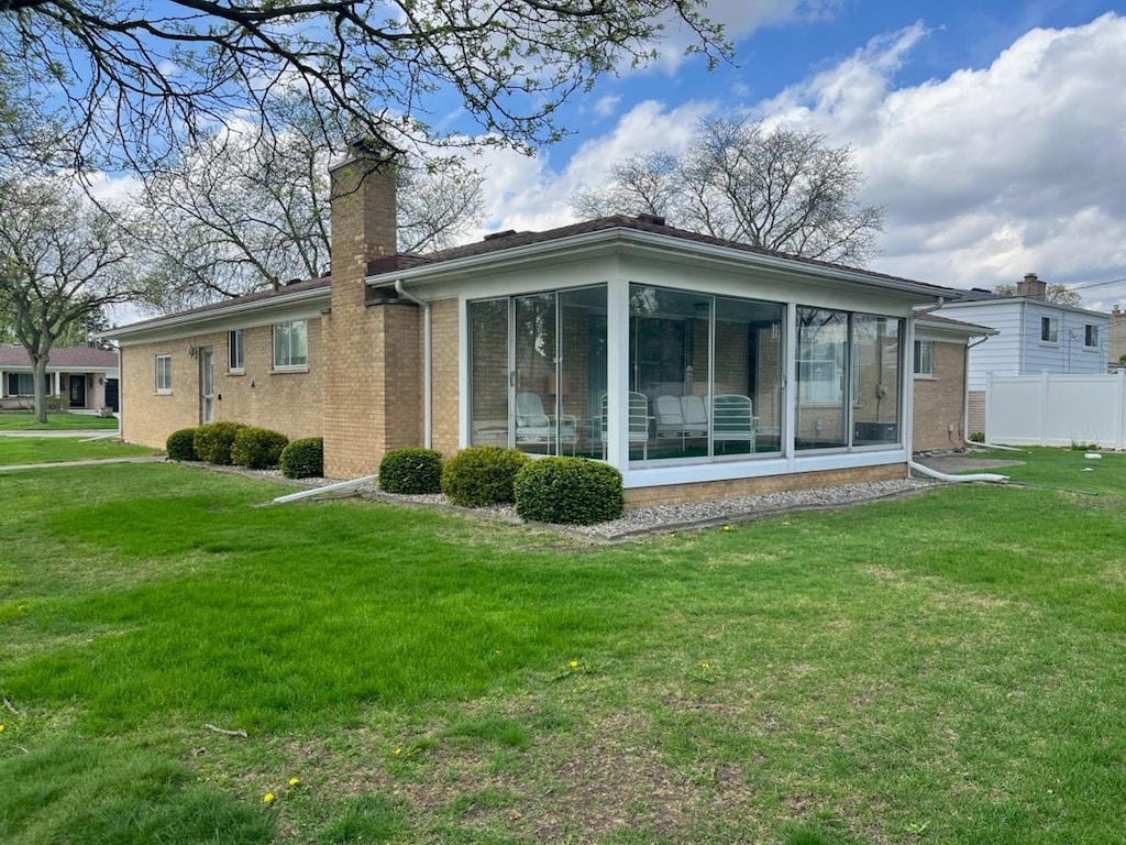 rear view of property with a yard, a sunroom, fence, and a chimney