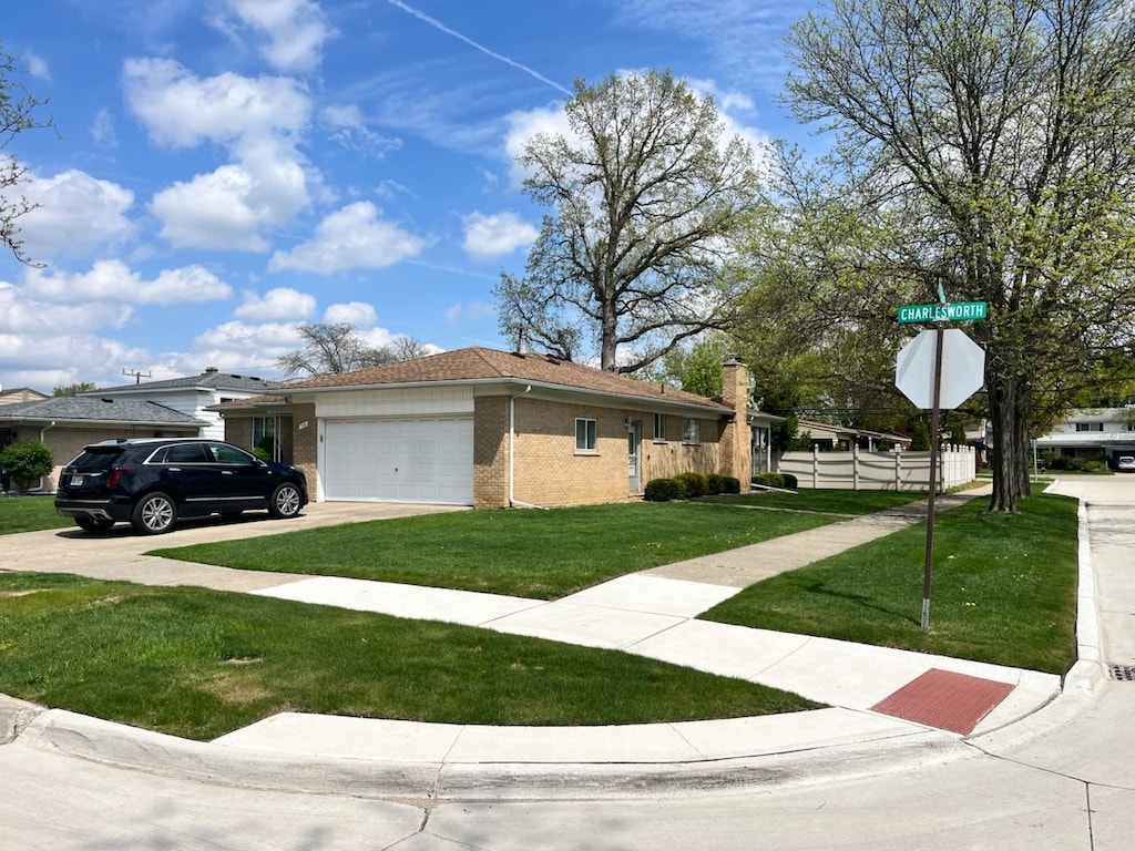 view of front of home with driveway, brick siding, fence, an attached garage, and a front lawn